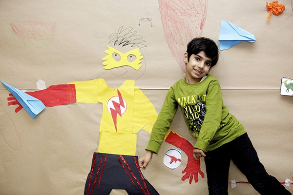 A young boy posing next to some superhero artwork