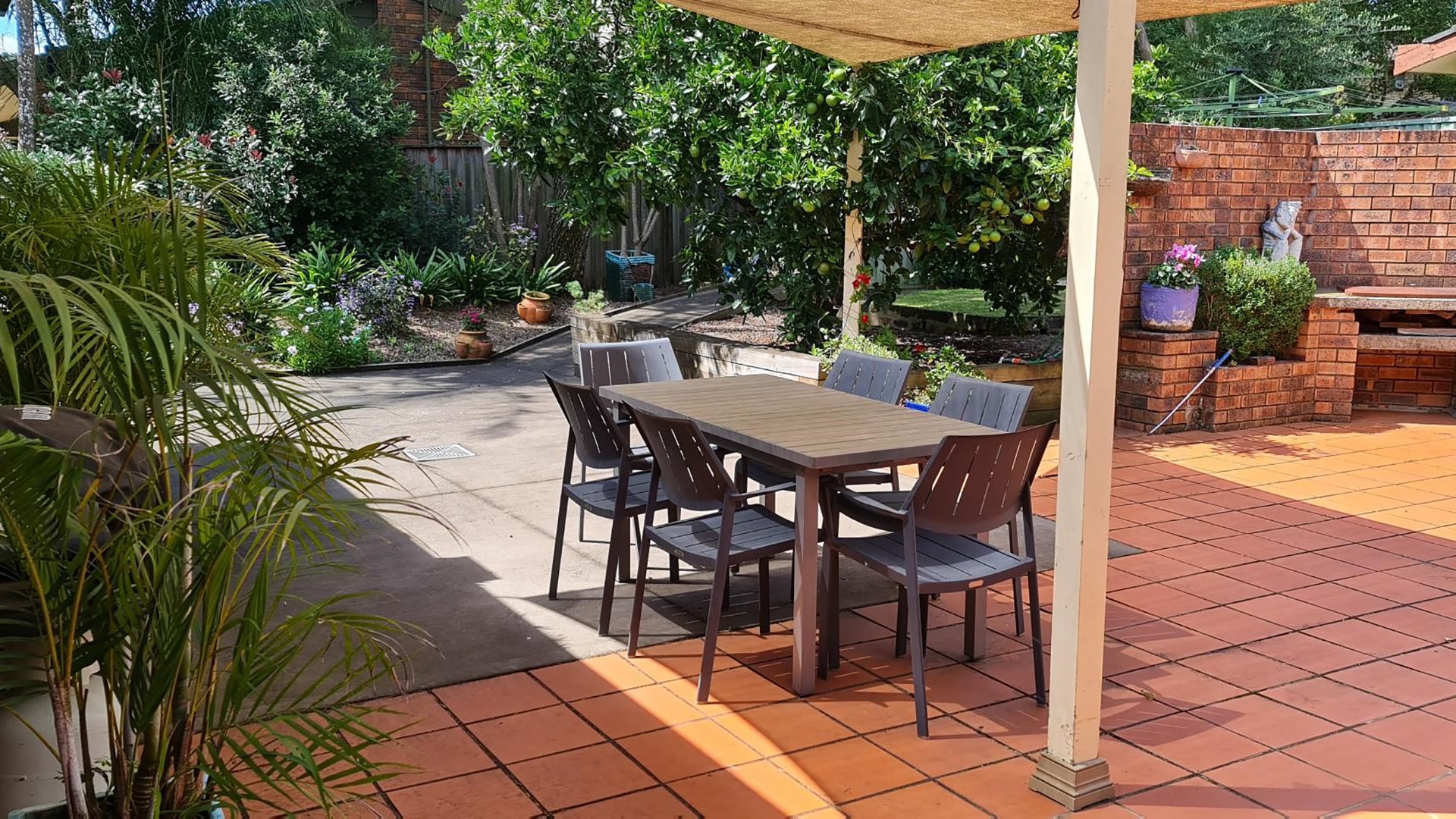View of the backyard with shaded dining area, garden beds and trees.