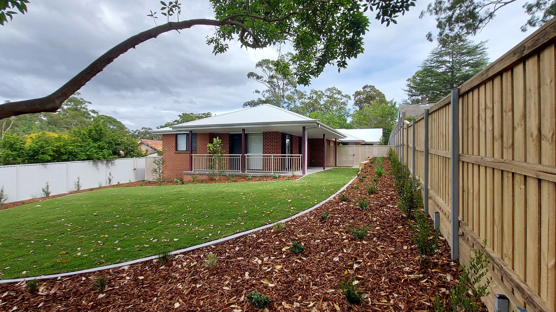 Front of Normanhurst 4 property, a large front garden with green grass sits infront of a red brick house.