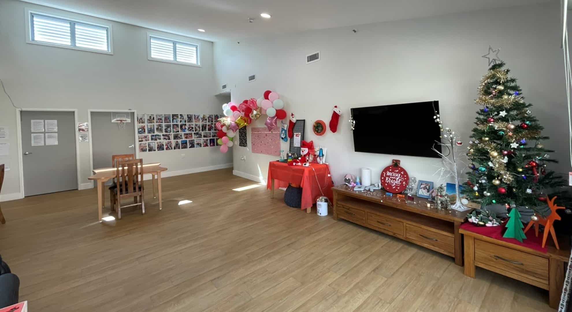 Large open living area with television, storage units, small table and chairs and a Christmas decorations and tree in the corner.