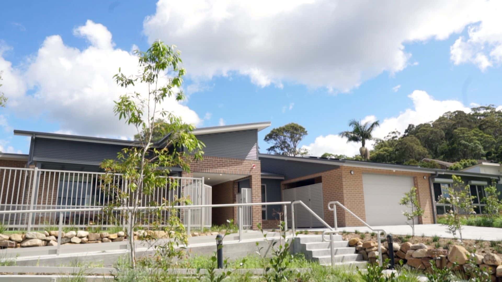 Front of the Wyong 1 property, a set of stairs with a ramp beside it leading up to a brick house with secure garage.