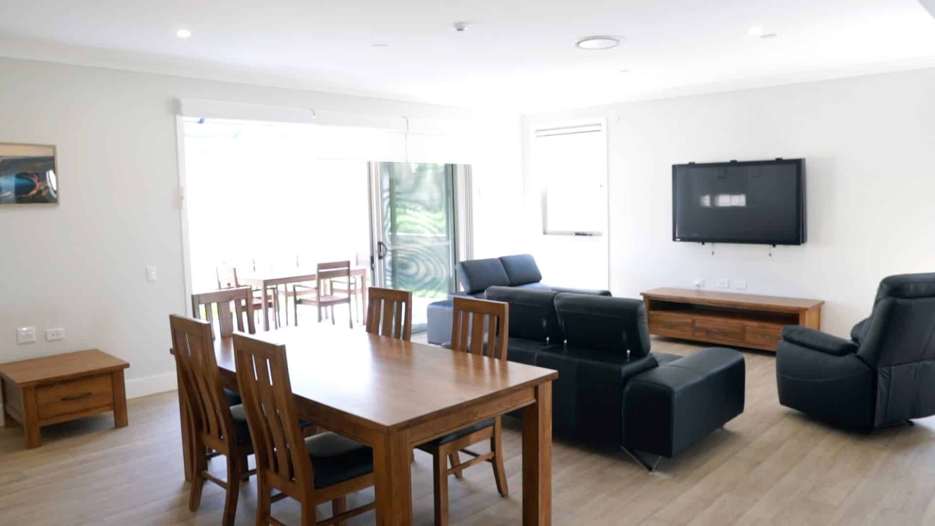 Living room at the Wyong 1 property featuring a tv with three couches, and dining table and glass sliding door out to a balcony