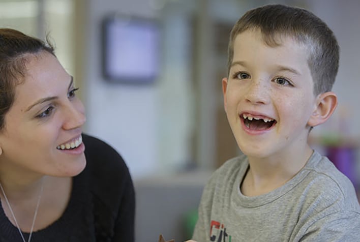 A woman looking at a young boy smiling, while he smiles towards the camera