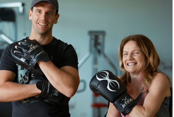 A man and lady smiling in a gym wearing boxing gloves.