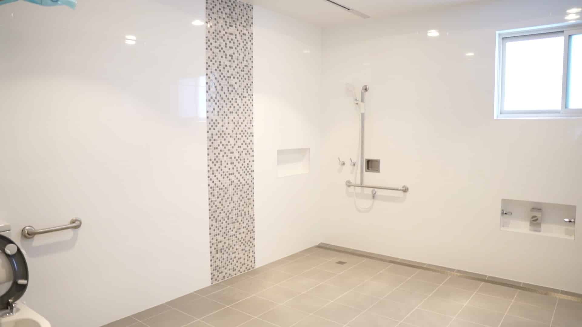View of a large bathroom with shower area, window and toilet.