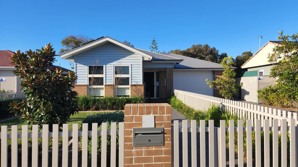 Front view of the Long Jetty 1 single story brick and wood paneled home.