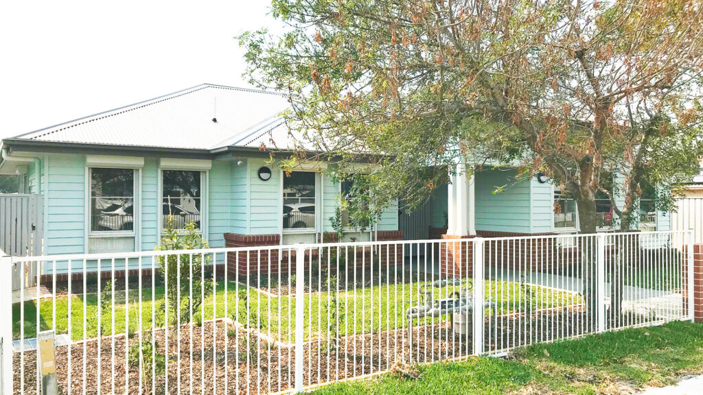 Front view of the brick and paneled home with fenced front yard.