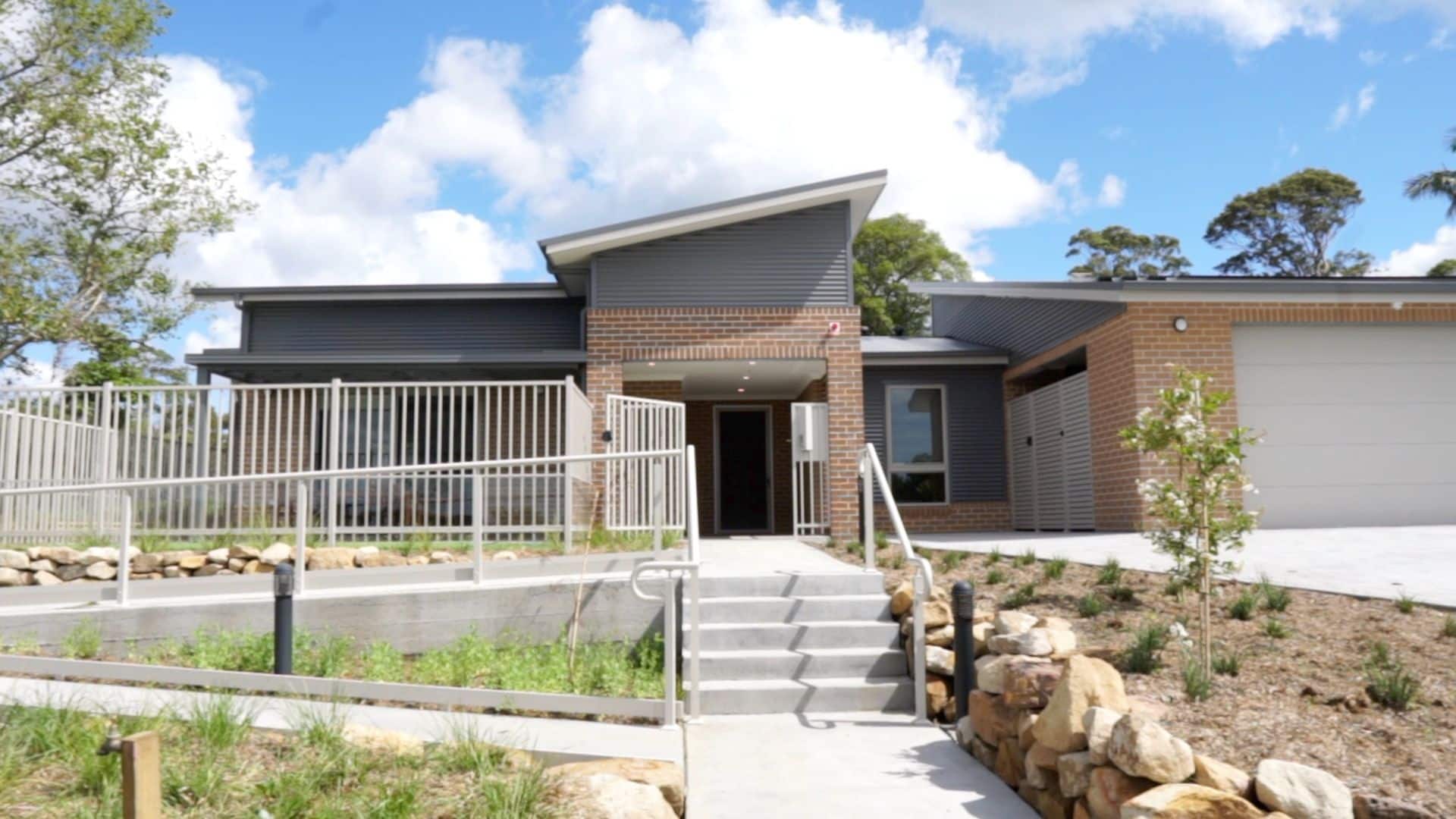 Front of the Wyong 1 property, a set of stairs with a ramp beside it leading up to a brick house.