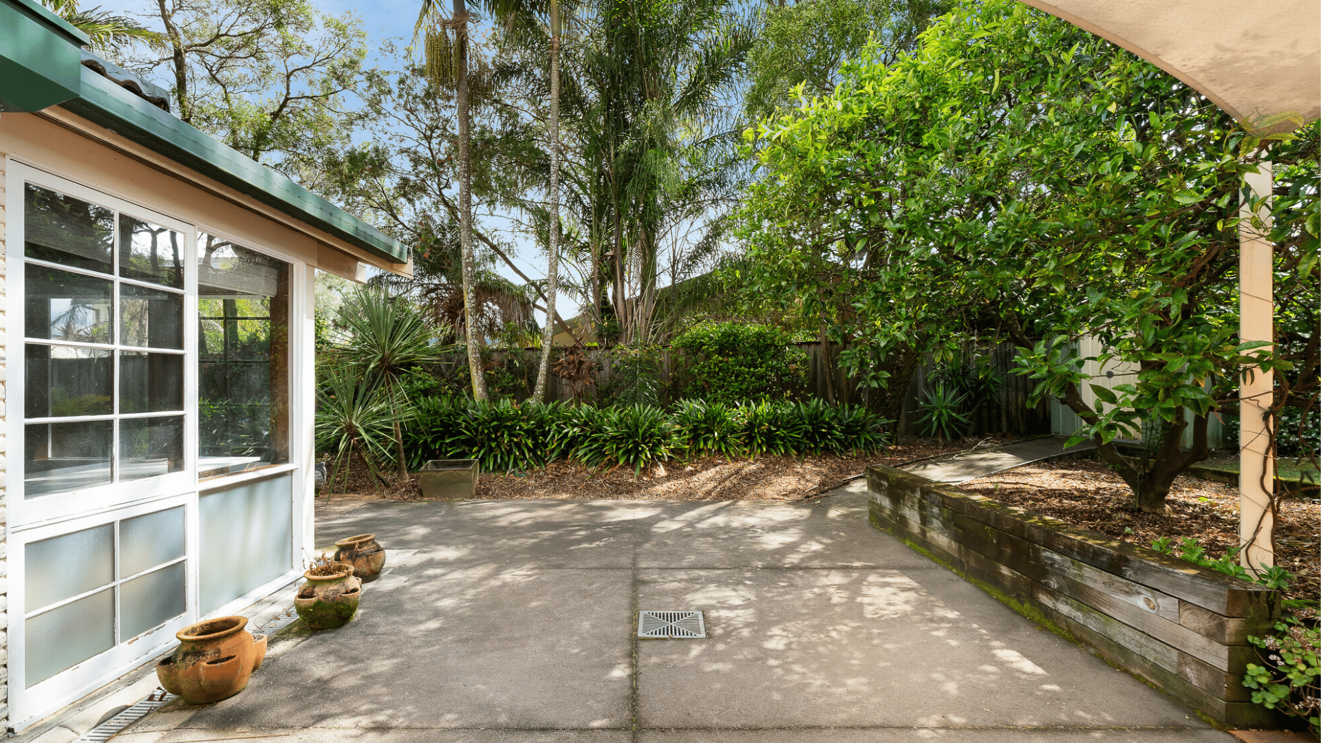 Outdoor area with a wide path, ramp access to a shed and garden beds filled with plants and trees