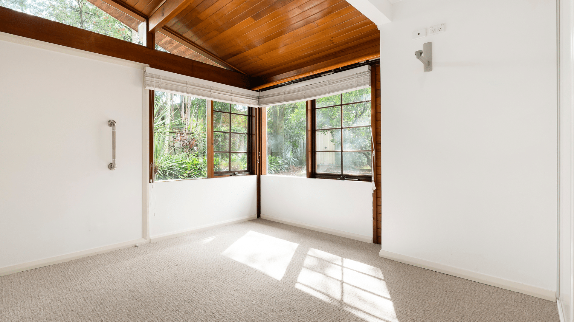 Spacious light filled bedroom with corner windows looking out to a garden and high ceilings.
