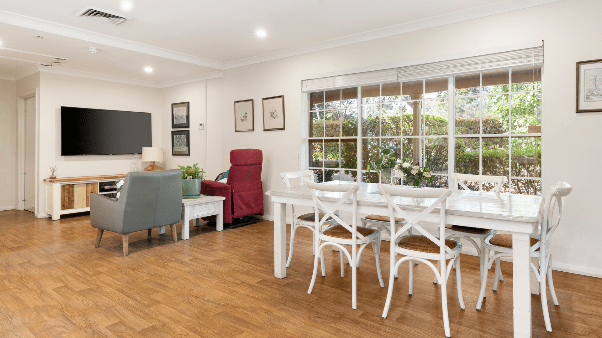 Living area divided into two spaces, with a long dining table next to a window and two couches in front of a large tv