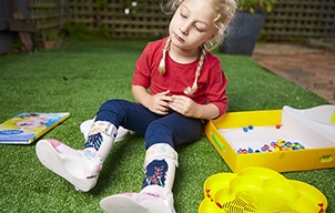 A young girl sitting on the ground playing wearing ankle-foot orthotics