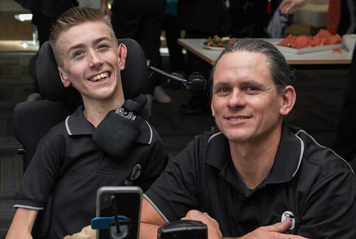 An male wheelchair user on the left and an another male on the right smiling to the camera. At the Remarkable event