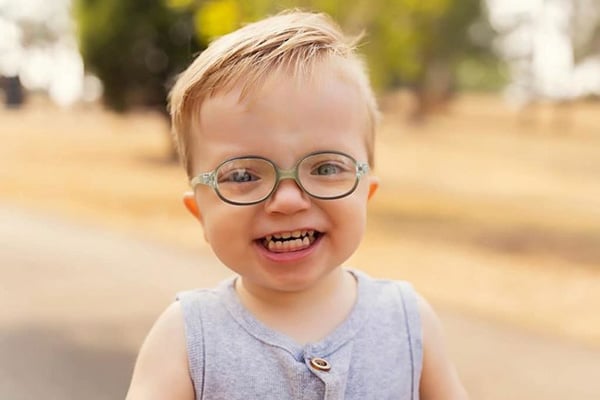 little boy in a grey singlet smiling and wearing glasses