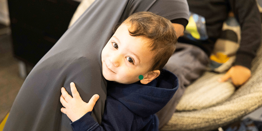 A small boy looking up and smiling to camera while he hugs his mother wearing a black hijab