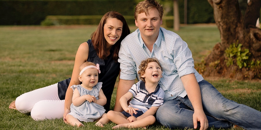 Pam and Tom Rogers sitting on the grass with their two children.
