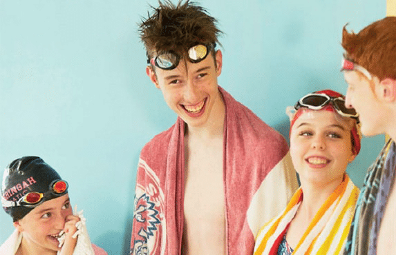 Four young people wearing swimwear and goggles standing together after swimming
