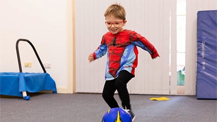 little boy wearing glasses and a spiderman top kicking a soccer ball