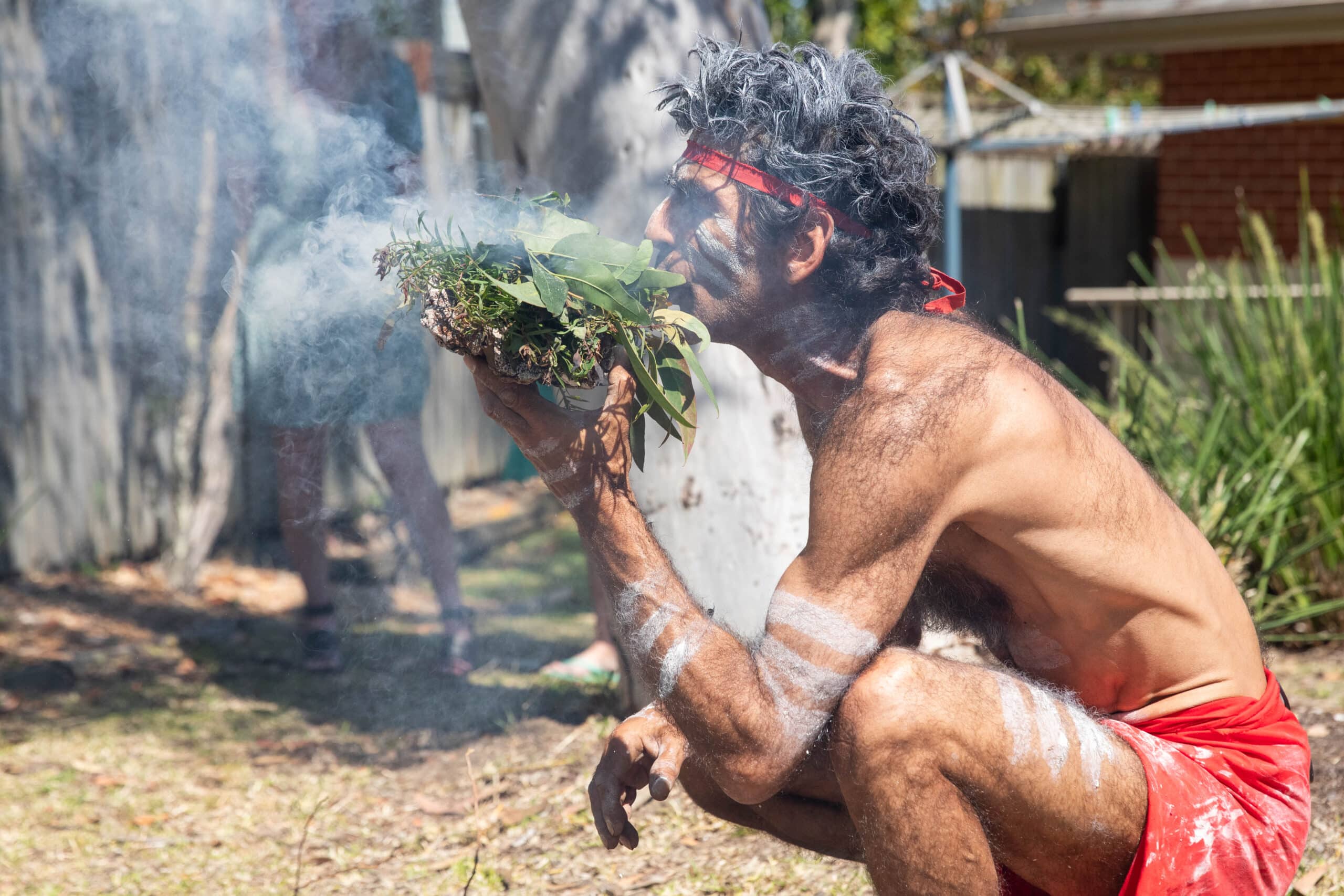 An Aboriginal man performing a smoking ceremony in traditional dress and body paint