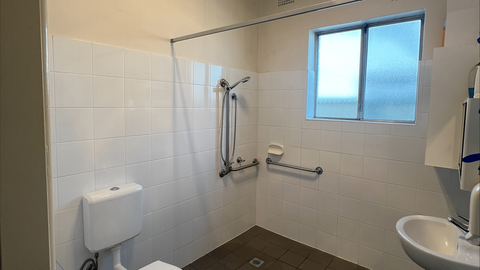 View of the bathroom showing a shower area next to a window, a toilet hand basin and storage cupboard.