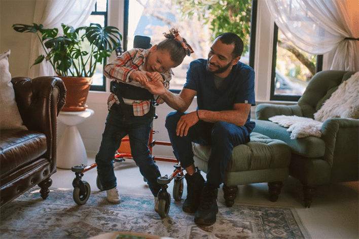 a father with his daughter standing in a walking frame in their living room