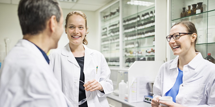 Three scientists wearing lab coats, having a discussion in a laboratory
