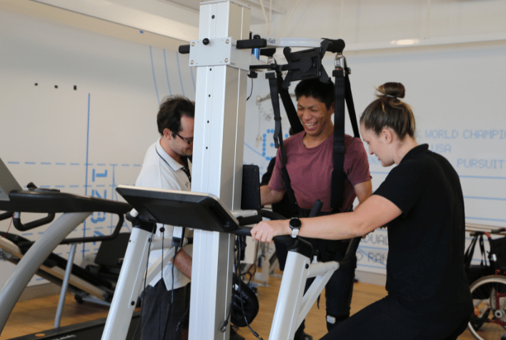 A male smiling using gym equipment with two therapists