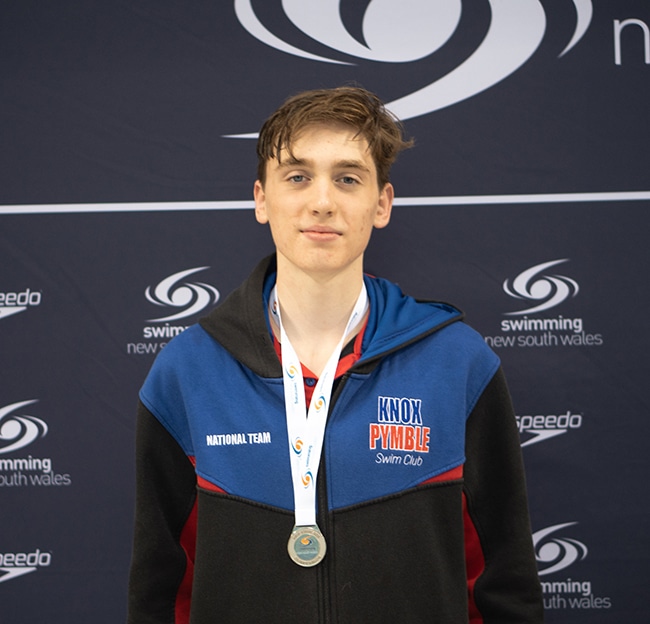 Liam Togher wearing a swimming medal looking at the camera.