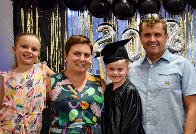 Family of four smiling to the camera. Ten year old girl dressed in graduation outfit.
