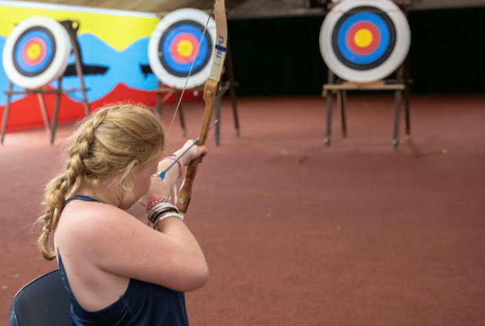 A female aiming a bow and arrow at a target