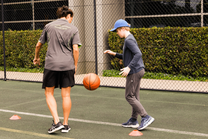 A young boy bouncing a basketball with a therapist outside.