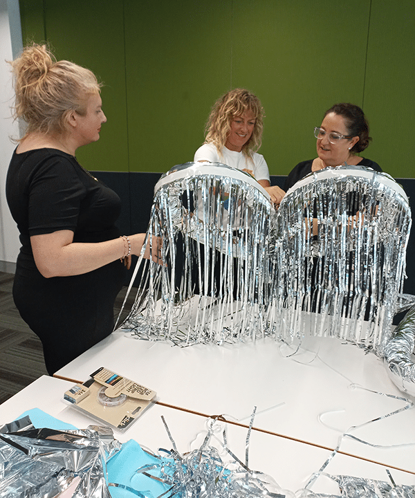 Three CPA staff members making large silver accessories for mardi gras