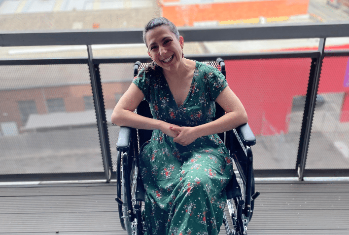 Woman with dark hair in wheelchair wearing green dress smiling