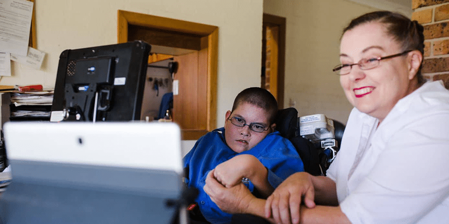 A young boy in a wheelchair with his mum in the middle of a telehealth session