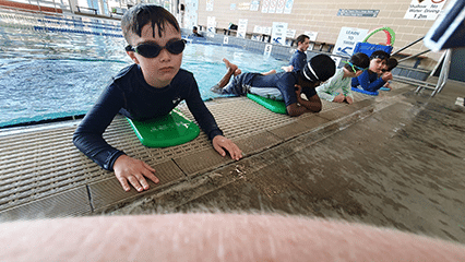 Boy in swimming pool wearing goggles with other kids in the background