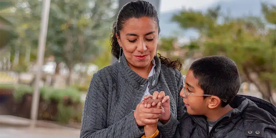 A tender moment as a boy with cerebral palsy holds his mother's hand during an outdoor interaction.