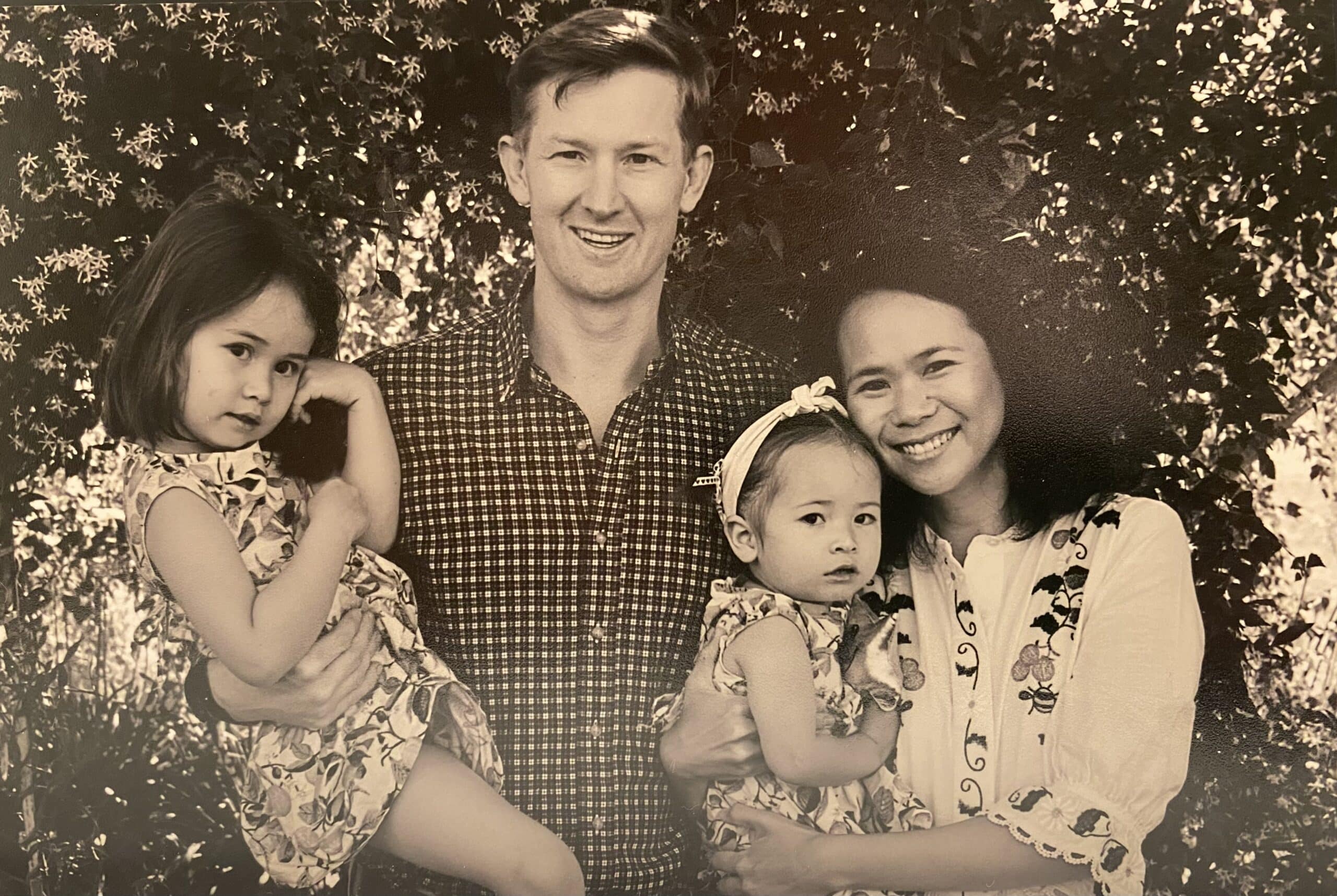 Black and white photo of a man and wife each holding one of their young daughters, smiling to camera