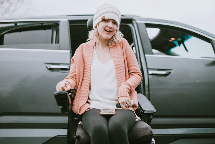 An independent young adult woman with cerebral palsy going about some of her daily routines. She rides her wheelchair up a ramp in her specially equipped van, preparing to drive to her job.