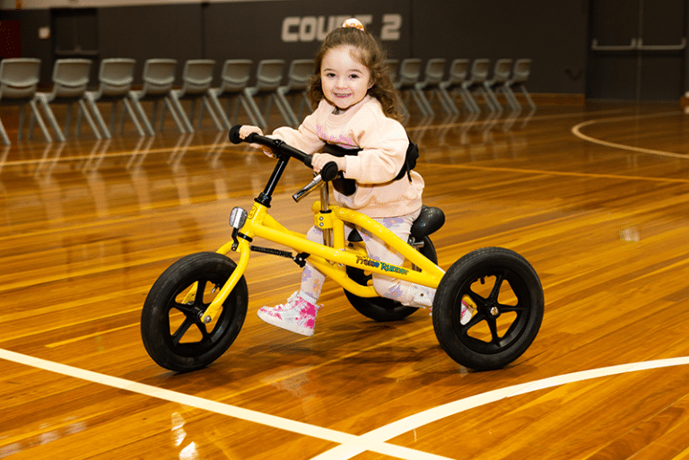 Quinn, smiling and running using her frame runner in a gym
