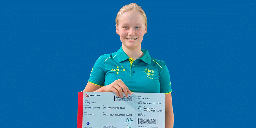 Paralympic swimmer Holly Warn holding an oversize plane ticket, smiling to camera