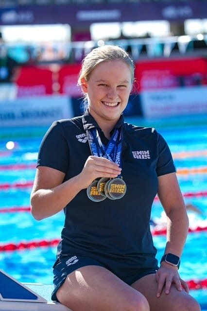 Holly Warn wearing medals around her neck, sitting in front of a pool smiling to camera