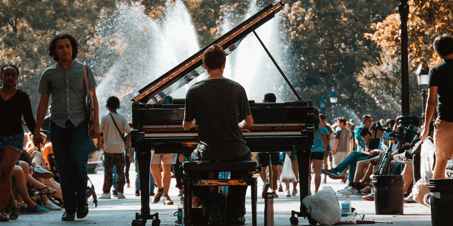 View from behind of a man sitting at a piano playing in the middle of a park