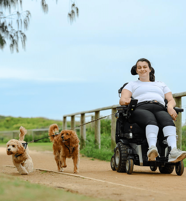 A female wheelchair user, walking two dogs along a path outside