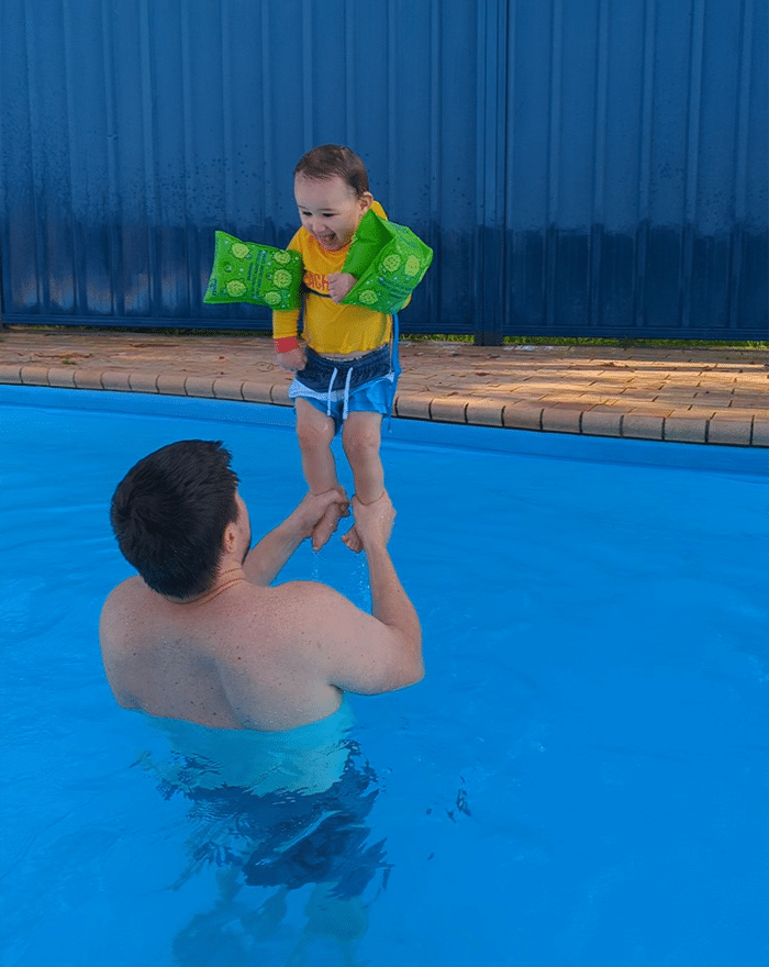 Baby Leo standing and balancing on his dad's hands while his dad standing in a swimming pool