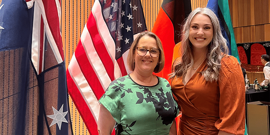 Cathy Morgan and Madison Paton standing in front of flags at the Australian embassy in DC.