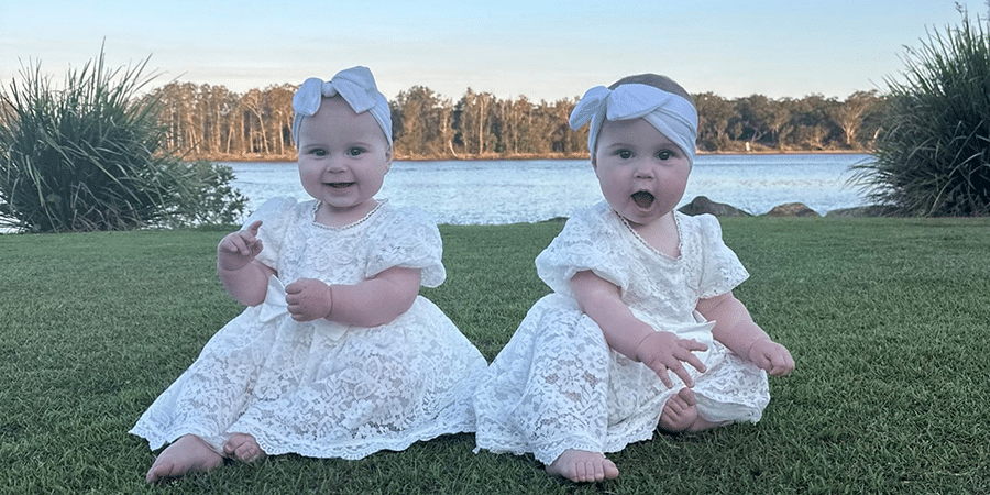 Twin baby girls Heidi and Sadie sitting on the grass in front of a lake.