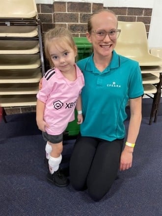 Tasmin kneeling down next to a young girl, smiling to camera