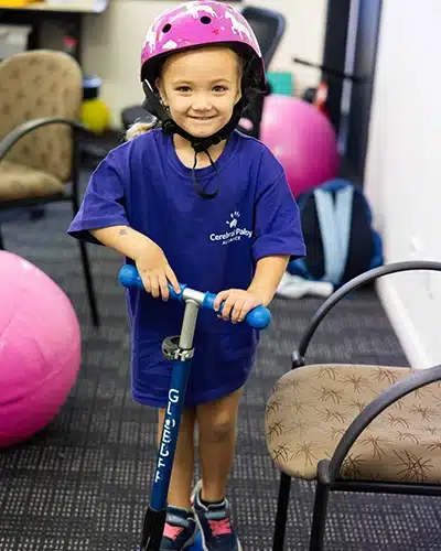 A young girl riding on a scooter.