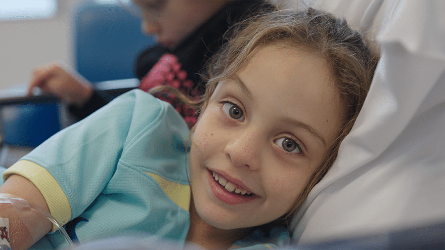 Zara smiling into the camera lying in bed during cord blood treatment.