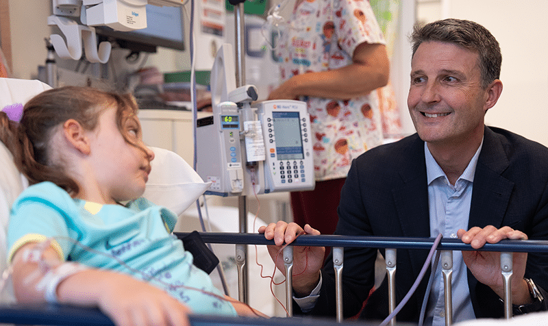Zara sitting in her hospital bed, talking to Professor Michael Fahey sitting next to her while receiving her umbilical cord blood infusion